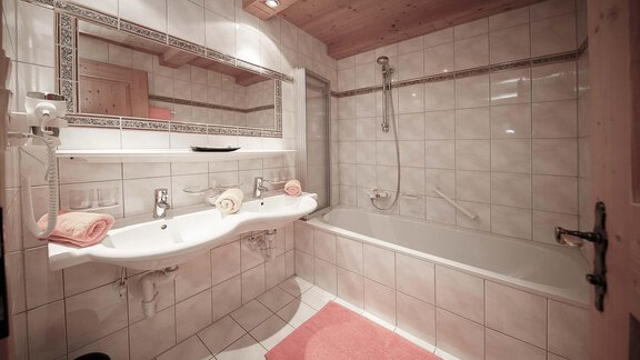 A modern bathroom with two sinks and a bathtub. The walls are tiled and there are soft towels on the sinks. - Haus Ingrid - Sölden
