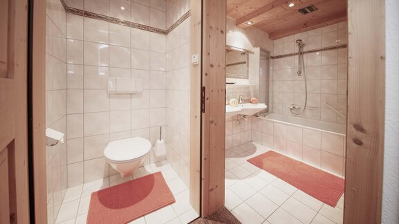A modern bathroom with bright tiles and wooden elements. There is a shower, bathtub, and a toilet, as well as a large mirror. - Haus Ingrid - Sölden
