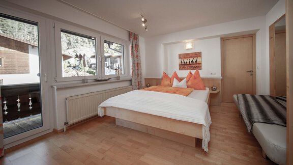 A modern bedroom with a large bed and orange cushions. Large windows offer a view of the surroundings. - Haus Ingrid - Sölden