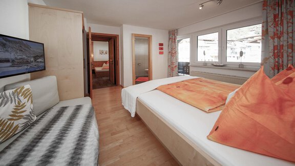 A cozy bedroom with a large bed and colorful pillows. The walls are light, and there is a TV as well as a large window that lets in natural light. - Haus Ingrid - Sölden
