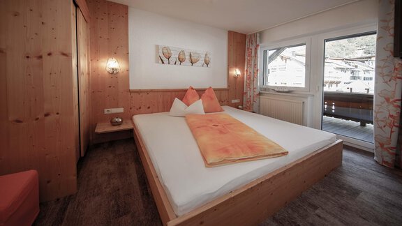 A modern bedroom with wooden paneling and large windows. It is warmly furnished with a large bed and decorative cushions. - Haus Ingrid - Sölden