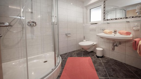 A modern bathroom with a shower and bright tiles. Towels and a rug in soft colors complement the decor. - Haus Ingrid - Sölden