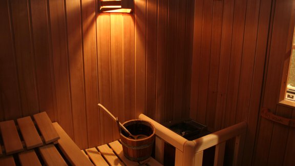 A cozy sauna with wooden walls and pleasant lighting. A bucket and a scoop are ready for the sauna experience. - Haus Rehwinkl - Sölden
