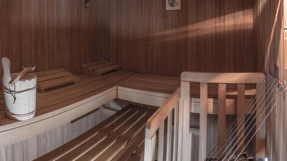A cozy sauna with wooden benches and a bucket for steam application. The wooden paneling creates a relaxing atmosphere. - Haus Tanja - Sölden