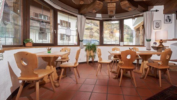 A cozy room with wooden chairs and tables. Large windows offer a view of the surrounding countryside. - Hotel am Hof - Sölden