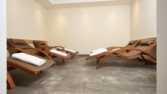 A quiet relaxation area with wooden lounge chairs and comfortable towels. The room is bright and designed in a minimalist style. - Hotel am Hof - Sölden