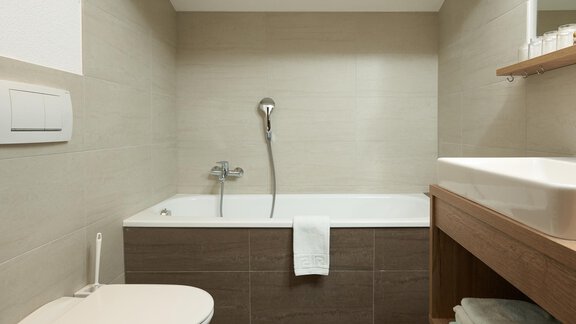 Modern bathroom with a bathtub and a wooden washstand. The walls are in neutral colors and the furnishings are simple and functional. - Hotel am Hof - Sölden