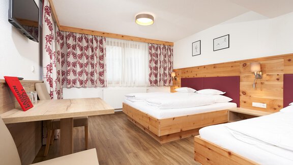 A bright, welcoming hotel room with wooden details and two beds. There is a table and a television on the wall. - Hotel am Hof - Sölden