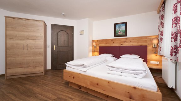 A cozy bedroom with a double bed and wooden paneling. There is a wardrobe and a window with curtains. - Hotel am Hof - Sölden