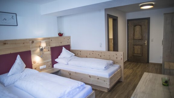 A cozy room with two wooden beds and modern design. The walls are bright, and there is a table as well as access to the door. - Hotel am Hof - Sölden