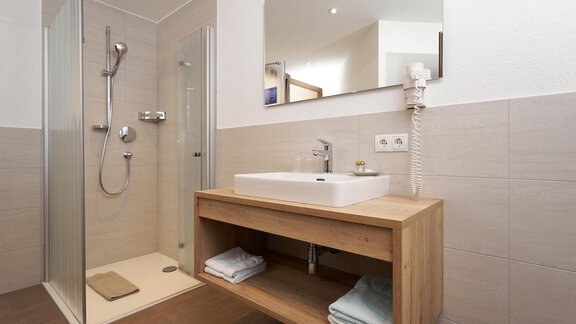 A modern bathroom with a shower and a wooden sink. Towels are neatly placed under the sink. - Hotel am Hof - Sölden