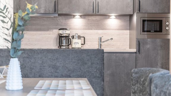A modern kitchen with gray cabinets and an elegant countertop. It includes a coffee machine, a faucet, and a microwave. - Landhaus Falkner - Sölden
