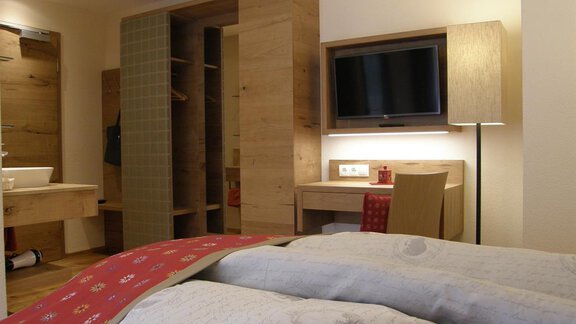 A cozy hotel room with wooden paneling and modern furnishings. There is a bed, a television, and a small desk. - Pension Sportalm - Sölden