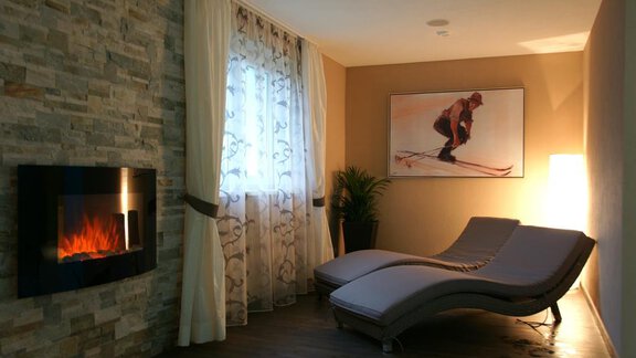A modern room with a cozy lounge chair, a fireplace, and an artistic wall decoration. The light is soft and creates a relaxed atmosphere. - Pension Sportalm - Sölden