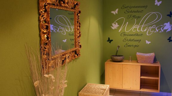 An inviting wellness area with a golden mirror frame and a green wall. Inspiring words are displayed on the wall, and there are elegant decorative elements. - Pension Sportalm - Sölden