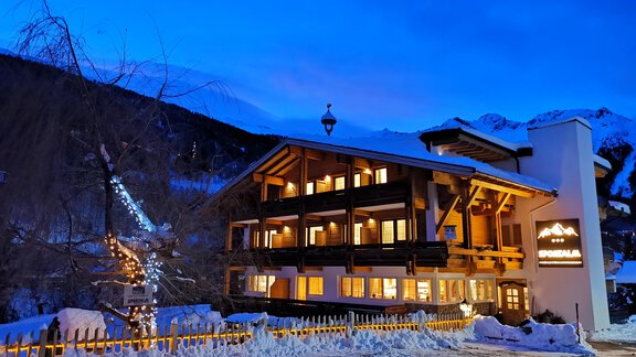A cozy hotel in the snow at twilight. The facade is beautifully lit and surrounded by mountains. - Pension Sportalm - Sölden