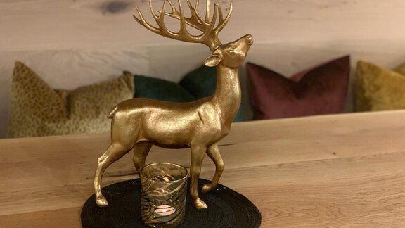 A golden deer figurine stands on a round placemat. In the background, cozy cushions can be seen. - Pension Sportalm - Sölden