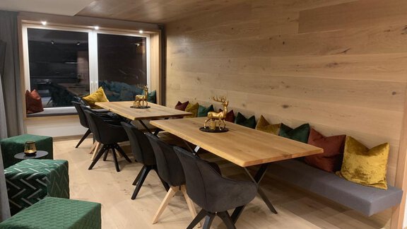 A modern dining area with a large wooden table and comfortable chairs. The walls are painted in warm wood tones, and colorful cushions create a cozy atmosphere. - Pension Sportalm - Sölden