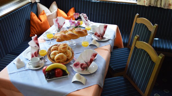 A beautifully set table with breakfast options, including rolls, fruit, and juices. The atmosphere is cozy with colorful cushions and a friendly decor. - Pension "Zur alten Mühle" - Sölden | © Carmen Waldhart