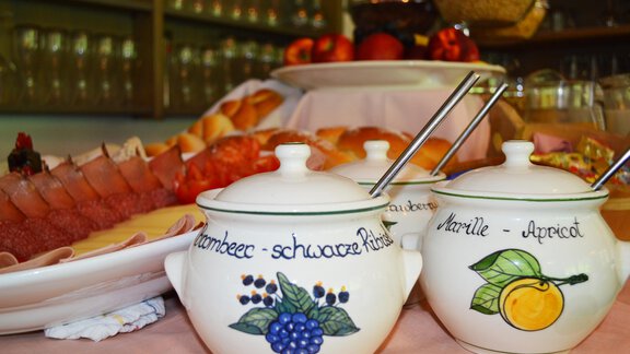An appealing breakfast table with cold cuts, fresh rolls, and fruit. Two decorative sugar bowls are in the foreground, one with blueberries and the other with apricots. - Pension "Zur alten Mühle" - Sölden | © Carmen Waldhart