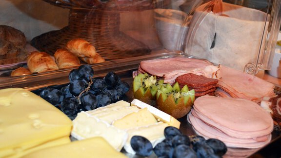A selection of cheese varieties and sausage, accompanied by fresh grapes and another fruit. In the background, filled rolls are visible. - Pension "Zur alten Mühle" - Sölden | © Carmen Waldhart