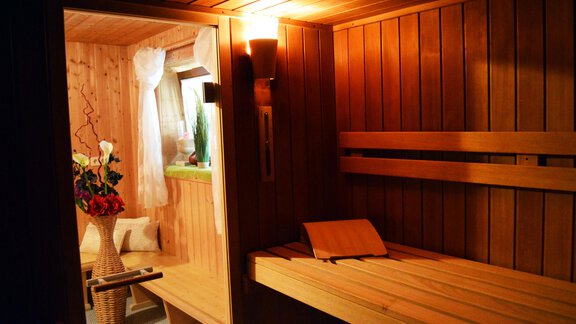 A cozy sauna with wooden paneling and soft lighting. In the background, there are plants and fresh flowers visible. - Pension "Zur alten Mühle" - Sölden | © Carmen Waldhart