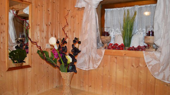 A cozy room with wooden paneling and a large window. In the center stands a decorative vase with colorful flowers. - Pension "Zur alten Mühle" - Sölden | © Carmen Waldhart
