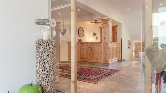 An inviting entrance area with a wooden counter and modern furnishings. Decorative elements like a chandelier and green apples create a cozy atmosphere. - Residenz Allegra - Sölden | © Residenz Allegra Sölden