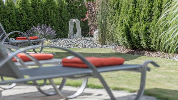 A beautiful garden with loungers and red cushions. In the background, there are green trees and decorative stones. - Residenz Allegra - Sölden | © Residenz Allegra Sölden