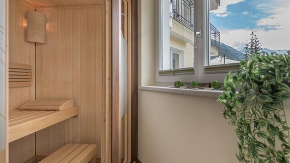 A cozy sauna with a wooden bench in a bright room. Large windows provide a view outside and let in plenty of light. - Residenz Allegra - Sölden | © Residenz Allegra Sölden