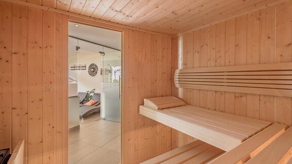 A bright sauna with wooden walls and a relaxation area. The entrance leads to a modern room with windows. - Residenz Allegra - Sölden | © Residenz Allegra Sölden