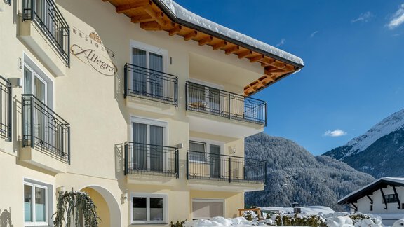 A charming building in alpine style, surrounded by snowy mountains. The clear sky and sunny atmosphere give the scene an inviting character. - Residenz Allegra - Sölden | © Residenz Allegra Sölden