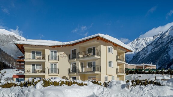 A cozy building amid a snowy landscape. Behind the house, impressive mountains stretch under a bright blue sky. - Residenz Allegra - Sölden | © Residenz Allegra Sölden