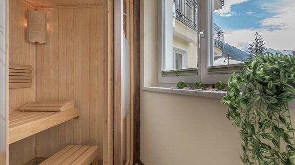A modern sauna with a wooden bench and a window that offers a beautiful view. There is also a green plant in the room. - Residenz Allegra - Sölden | © Residenz Allegra Sölden
