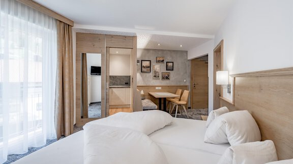 A modern hotel room with a large bed and bright wood design. There is a table and chairs as well as a large balcony with plenty of light. - Residenz Allegra - Sölden