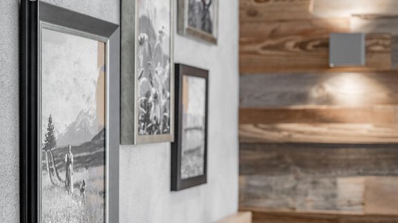 A modern interior with black-and-white pictures in frames on a gray wall. In the background, wooden elements are visible, adding coziness to the room. - Residenz Allegra - Sölden