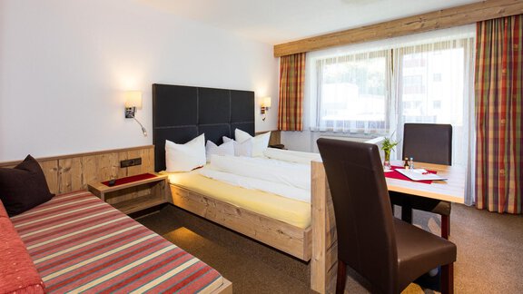 A cozy hotel room with a double bed and a seating area. Large windows provide plenty of daylight. - Sportpension Rubin - Sölden