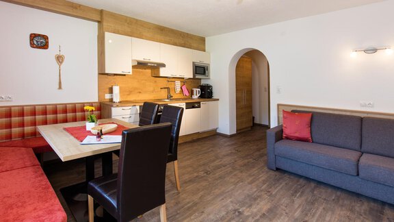 A modern kitchen corner with wooden and white cabinets. The living area is comfortably furnished with a sofa and a dining table. - Sportpension Rubin - Sölden