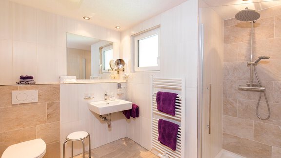 A modern bathroom with a shower and a sink. White walls and fluffy purple towels create an elegant atmosphere. - Sportpension Rubin - Sölden