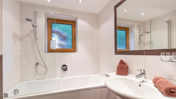 A modern bathroom with a bathtub and a sink. It has bright tiles and a window that lets in daylight. - Vizensn Living - Sölden