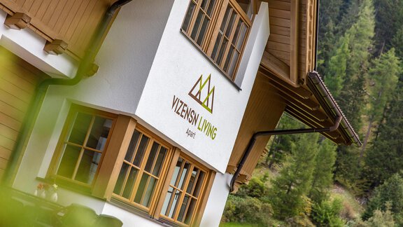 A modern facade of a building with large windows and a green logo. Surrounded by a beautiful, natural environment. - Vizensn Living - Sölden