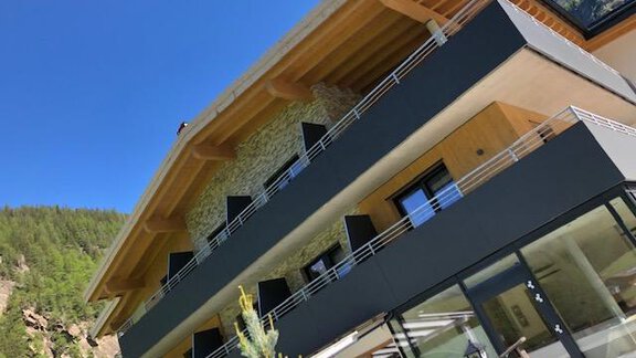 A modern building with wooden and concrete accents. It is surrounded by green mountains under a blue sky. - Gasthof Brückenwirt - Zwieselstein