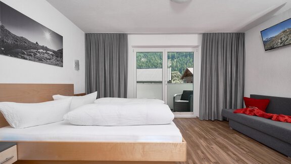 A modern bedroom with a double bed and a cozy sofa. Large windows with curtains offer a view outside. - Apart Alessandro - Huben