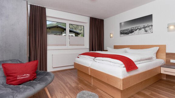 A cozy bedroom with a large bed and warm wooden floor. The room is modernly furnished and has a window overlooking the mountains. - Apart Alessandro - Huben