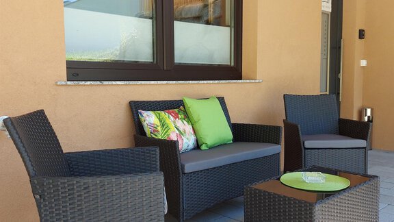 Relaxing outdoor seating area with a black rattan furniture set. A table with a green decorative bowl and colorful cushions creates a cozy atmosphere. - Apart Montis - Längenfeld