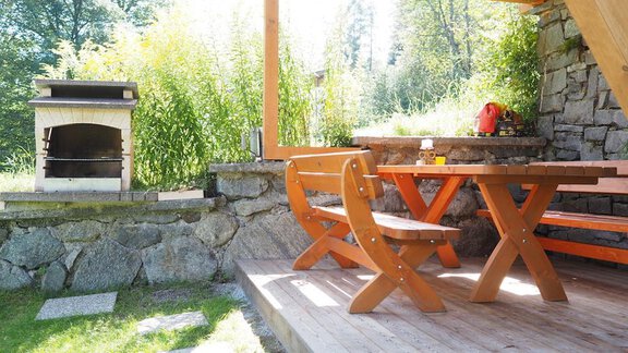 Ein gemütlicher Außenbereich mit einem Holztisch und Bänken. Im Hintergrund befindet sich ein Steingrill und üppige grüne Pflanzen. - bei Herrmann´s - Sautens | © Jessica Herrmann