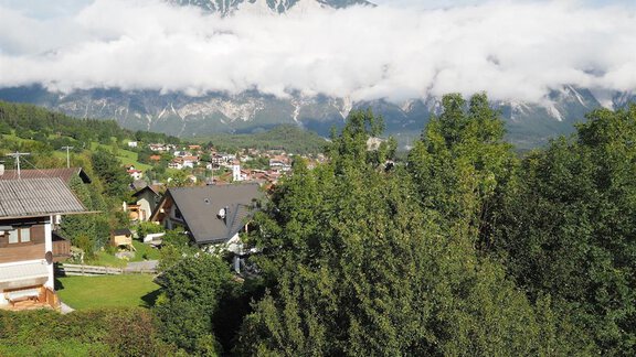 Eine malerische Landschaft mit grünen Bäumen und Häusern in einer ländlichen Umgebung. Im Hintergrund erheben sich majestätische Berge unter einem Wolkenhimmel. - bei Herrmann´s - Sautens | © Jessica Herrmann