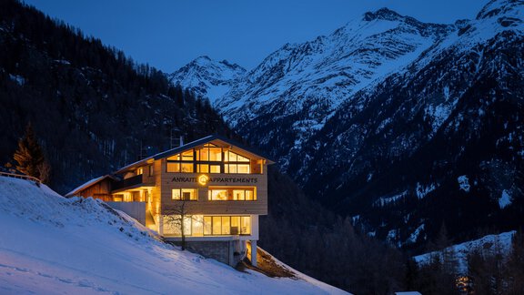 A modern house in the mountains, surrounded by snow. The lighting in the evening creates a cozy atmosphere. - Anraitl Appartements Sölden - Sölden