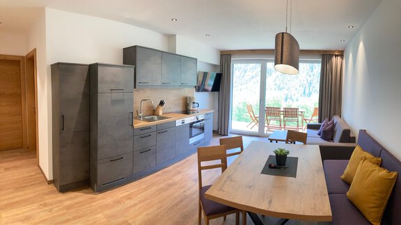 A modern kitchen with a dining area and a living room. Large windows offer a view of the terrace and the outdoor area. - Anraitl Appartements Sölden - Sölden