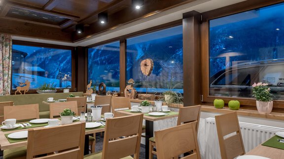 A cozy restaurant with wooden furniture and large windows. The view outside reveals a picturesque mountain landscape. - Apart Hotel Garni Wieser - Sölden